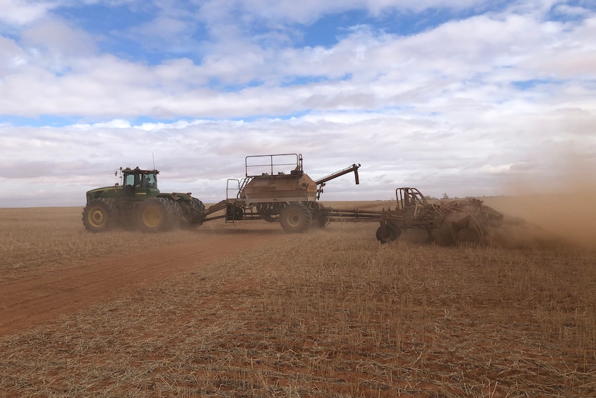 A tractor moves through a dry and dusty paddock sowing barley
