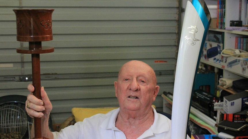 old bald man sitting with two Olympic torches