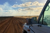 The passenger side of a ute in foreground with dust kicking up behind a vehicle on dirt road in the distance