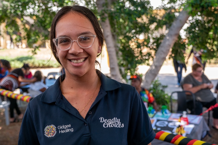 A smiling young woman wearing glasses stands outdoors. 