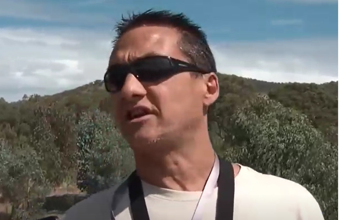 Screengrab from footage of Dezi Freeman wearing sunglasses and gesturing while speaking with police.