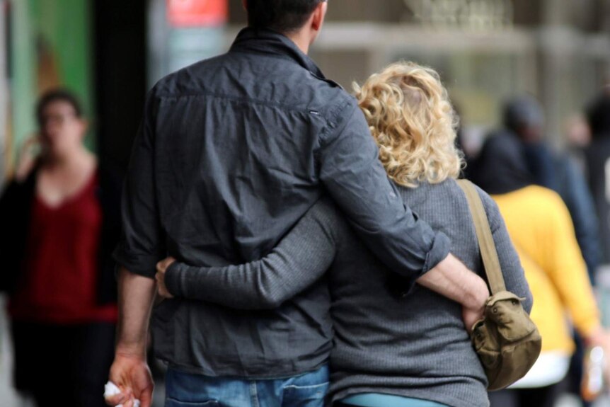 Tall man and shorter woman with arms around each other while walking.