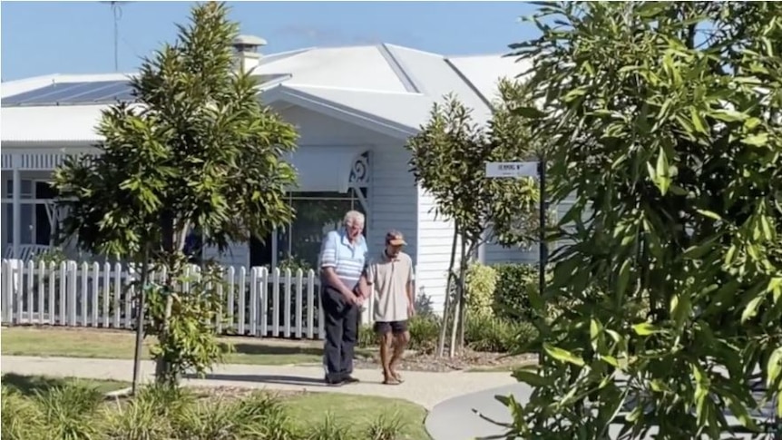A person walks with an elderly man through an aged care facility designed to look and feel like a small town.