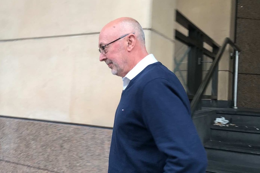 A bald man with glasses walking outside a court house.