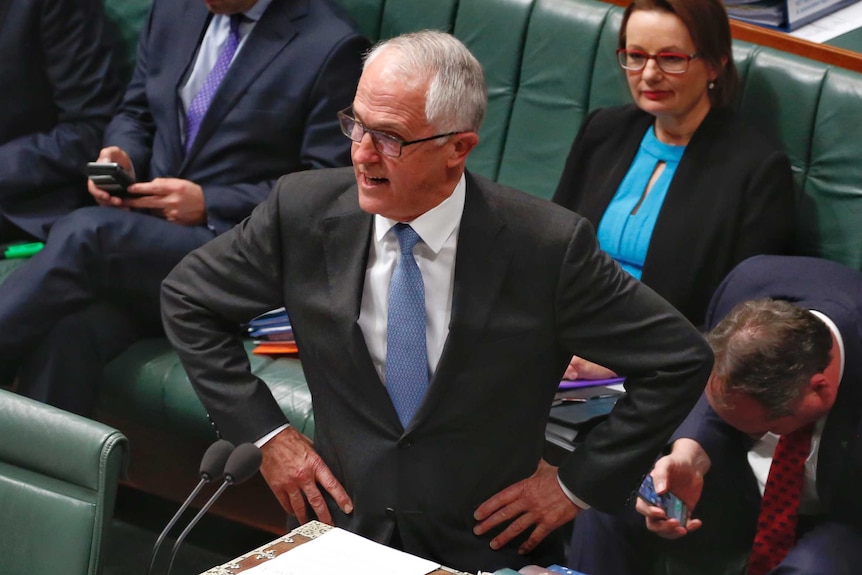 Man wearing suit stands with hands on hips while speaking