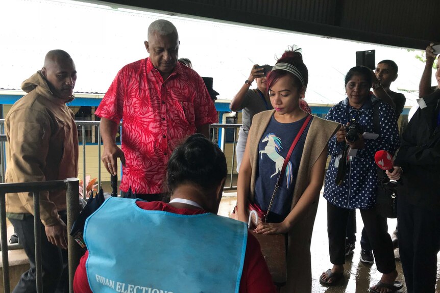 Fiji's Prime Minister Frank Bainimarama at a polling place during the 2018 election. Journalists are taking photos of him.