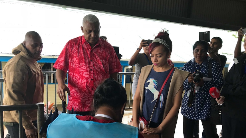 Fiji's Prime Minister Frank Bainimarama at a polling place during the 2018 election. Journalists are taking photos of him.