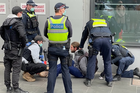 A man sitting on the ground in handcuffs surrounded by police.