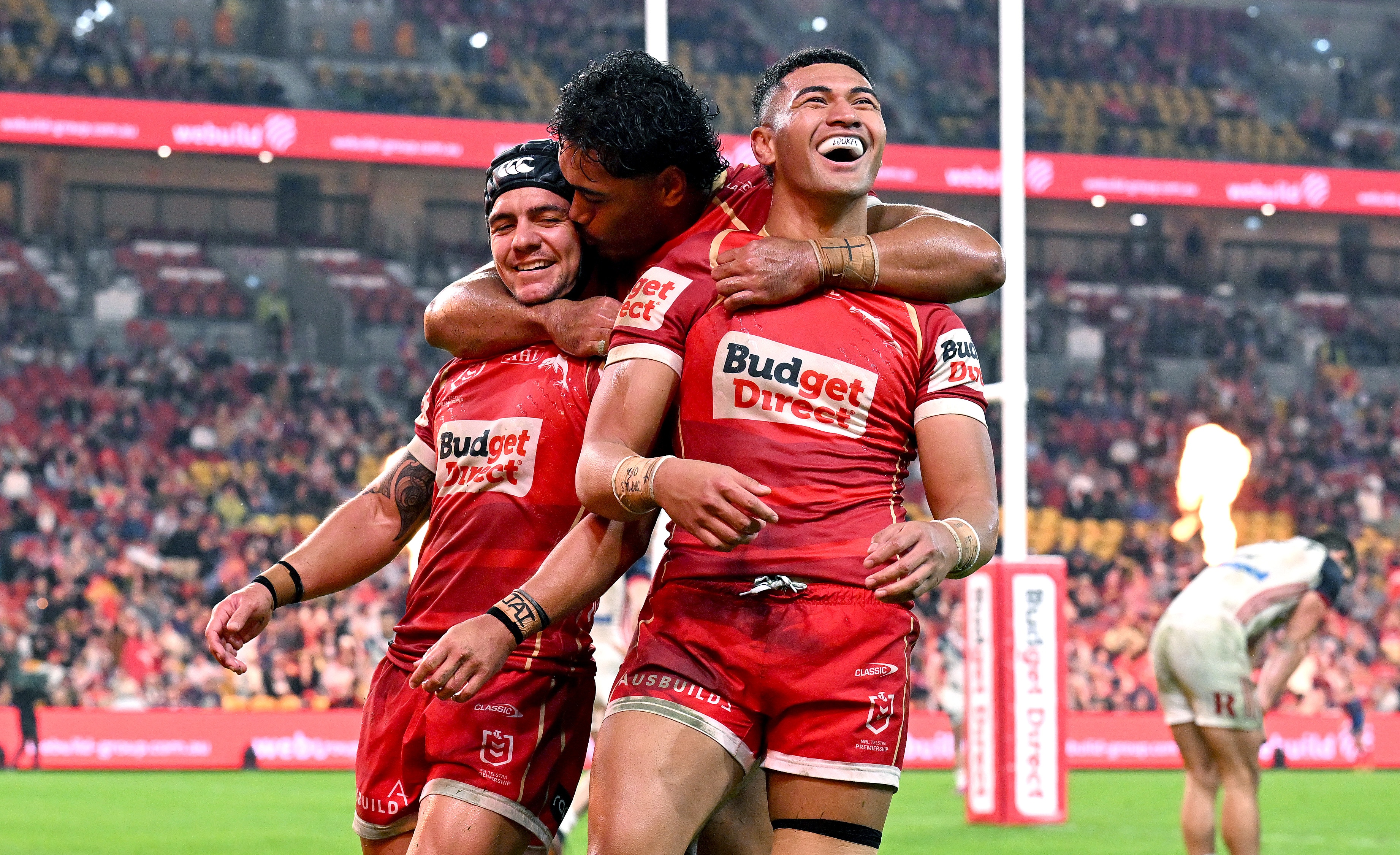 A rugby league player in red is hugged by his teammates while celebrating a try