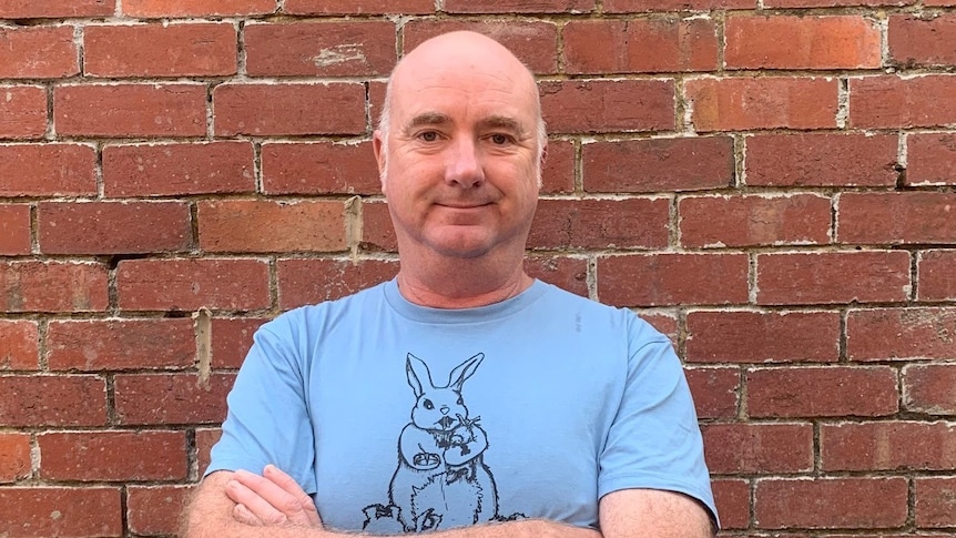 Andrew Brassington stands in front of a brick wall in a t-shirt with a bunny on it