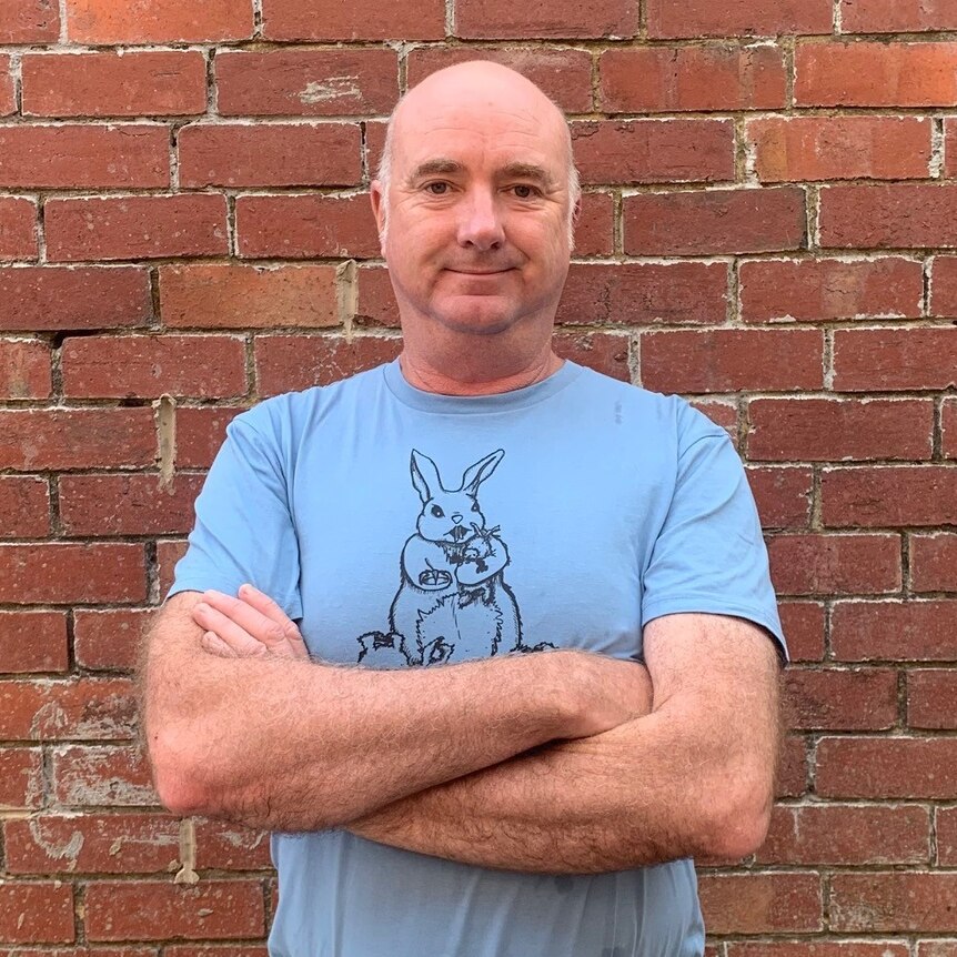Andrew Brassington stands in front of a brick wall in a t-shirt with a bunny on it