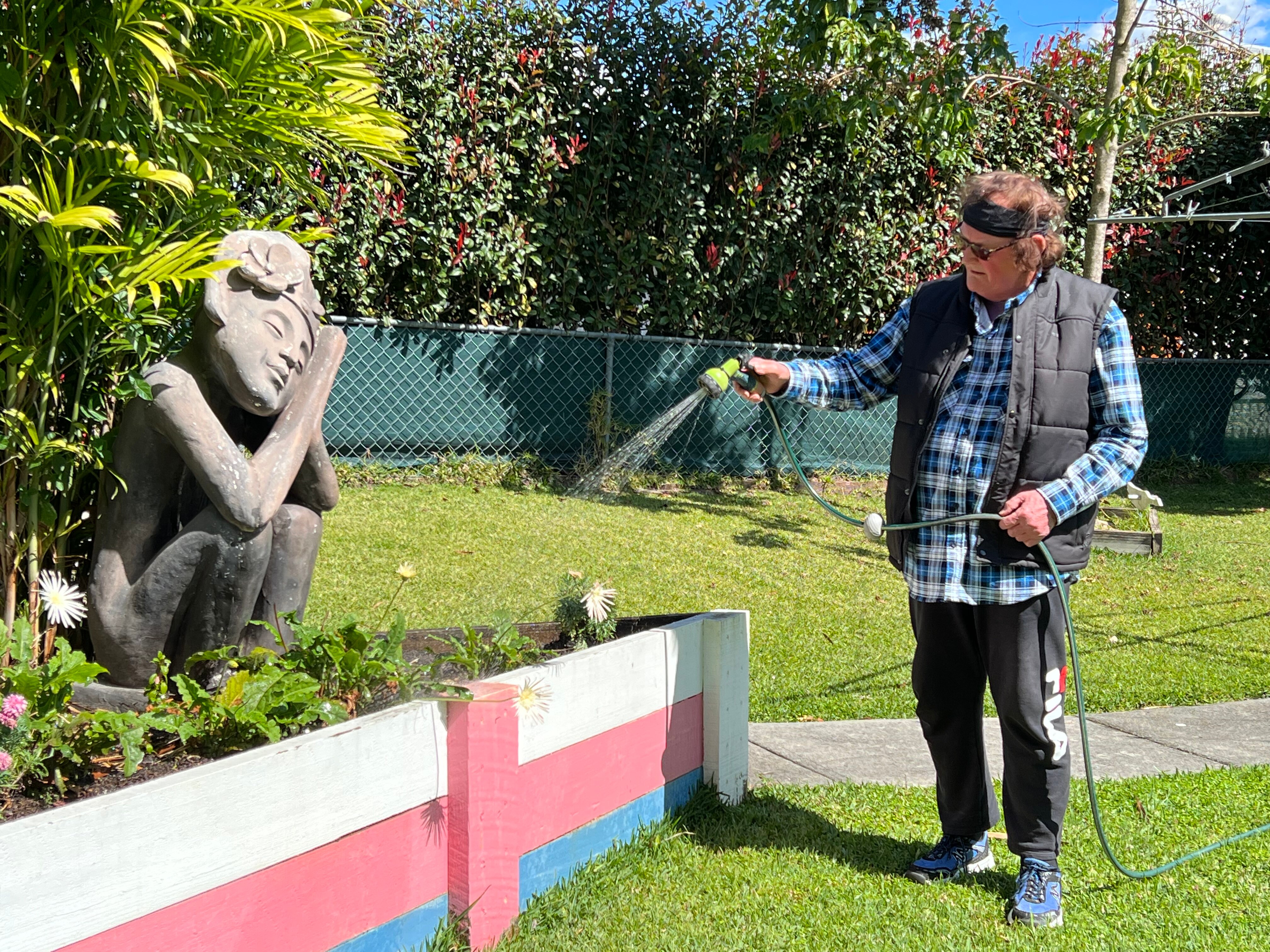 Gina Mather watering her garden , blue, white and pink paint on the retaining wall