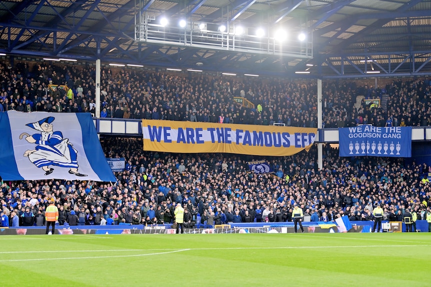 A banner that reads "WE ARE THE FAMOUS EFC" hangs in a packed football stadium