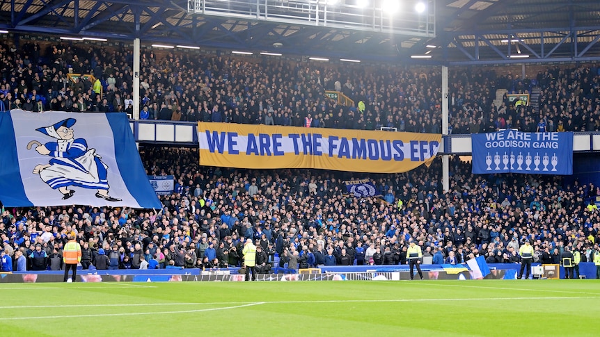 A banner that reads "WE ARE THE FAMOUS EFC" hangs in a packed football stadium