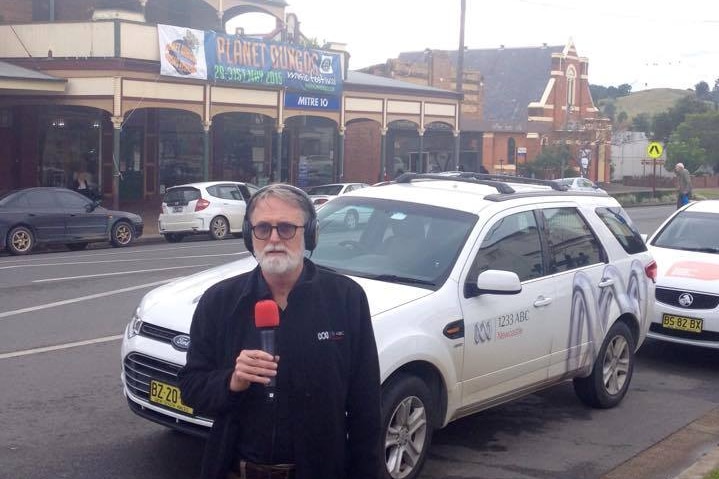 Paul Bevan holding microphone standing in front of ABC car in Dungog street.