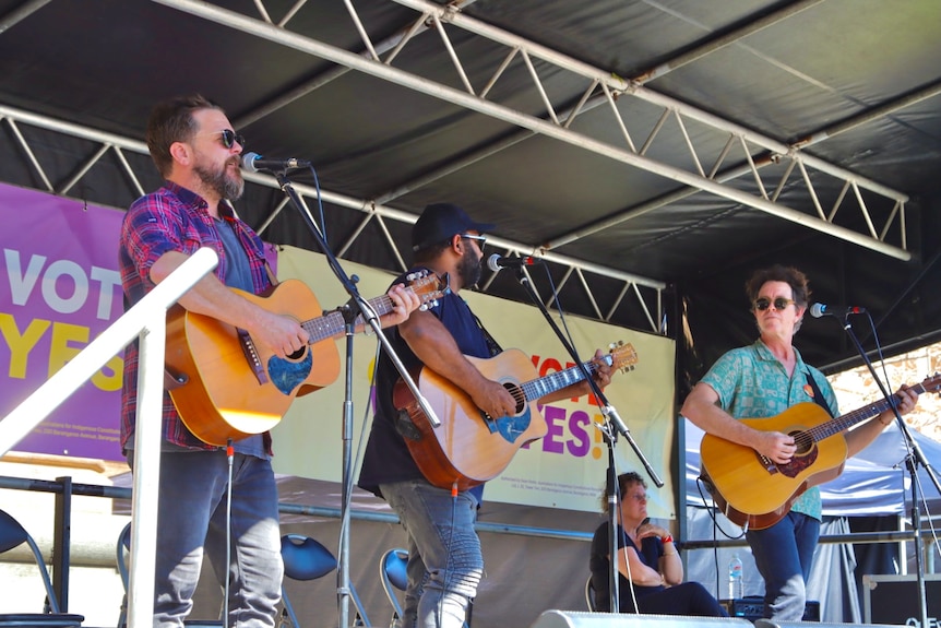 three musicians singing on stage holding guitars