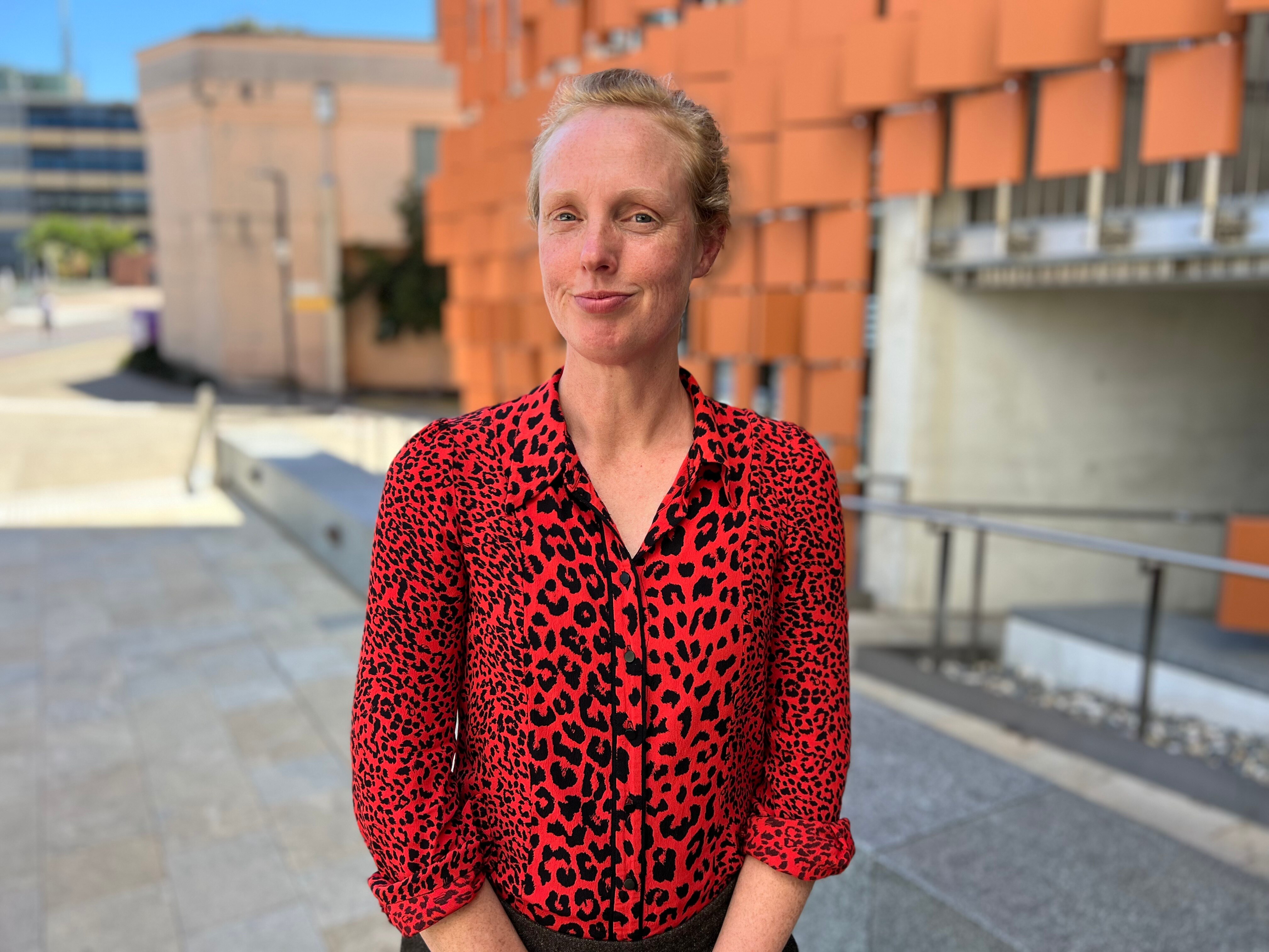 A woman wearing a red shirt looks at the camera and smiles
