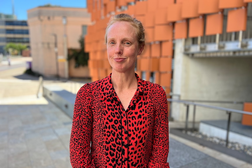 A woman wearing a red shirt looks at the camera and smiles