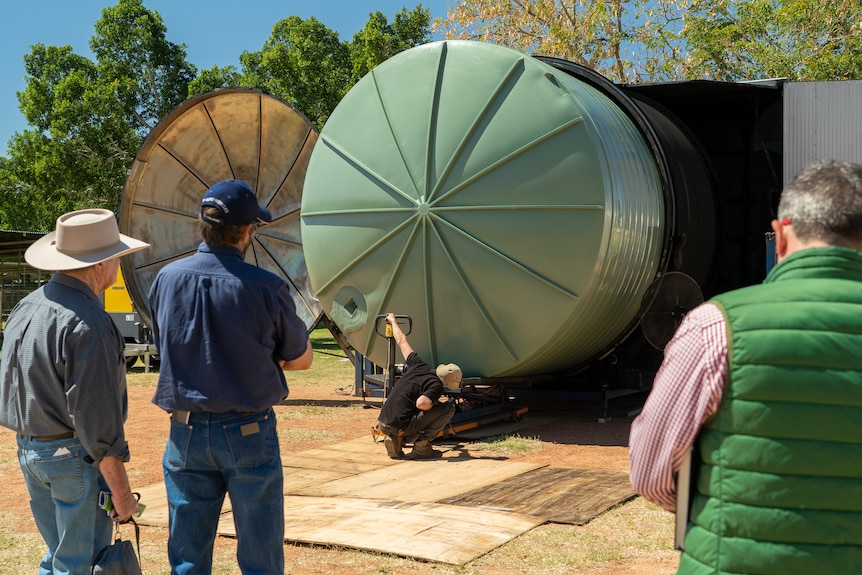 Three man watch on as one man crouches down and pulls a water tank out of an enormous mould onto a transportation trolley.