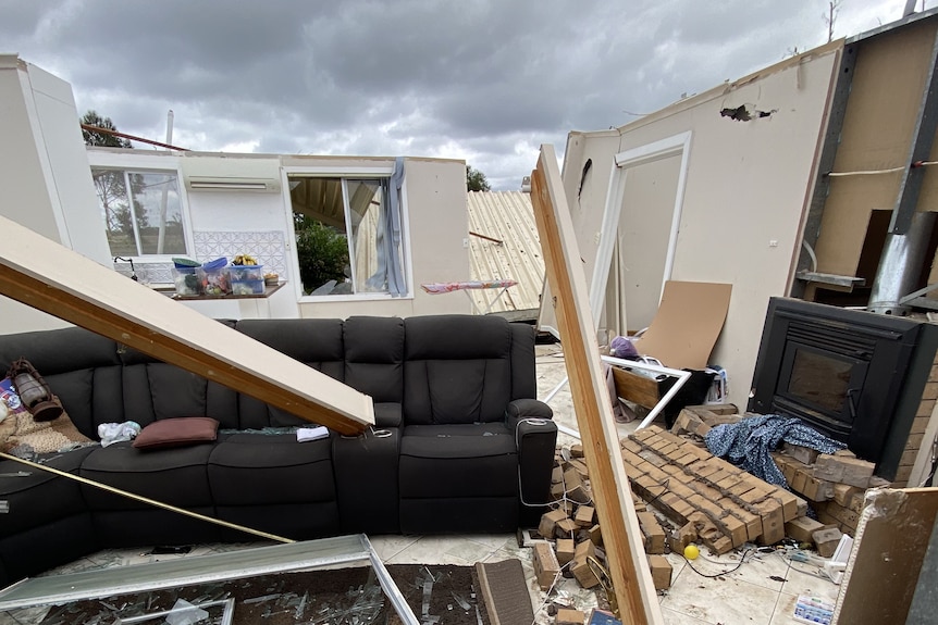 A room that has been destroyed, with walls leaning away, no roof and debris covering furniture.