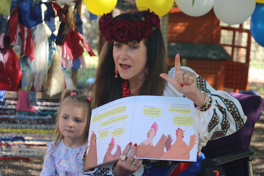 A lady wears a crown of roses and holds a children's book