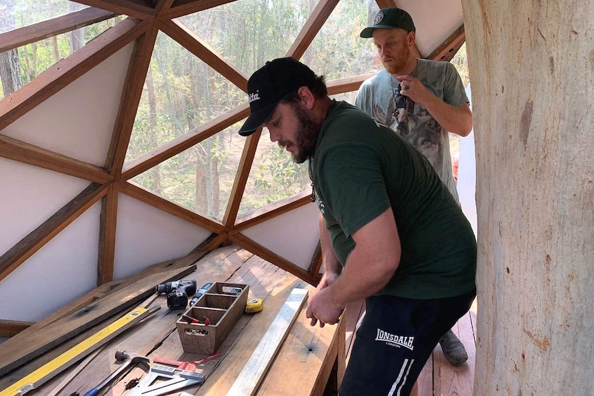 Two men with carpentry tools bulding a tree house