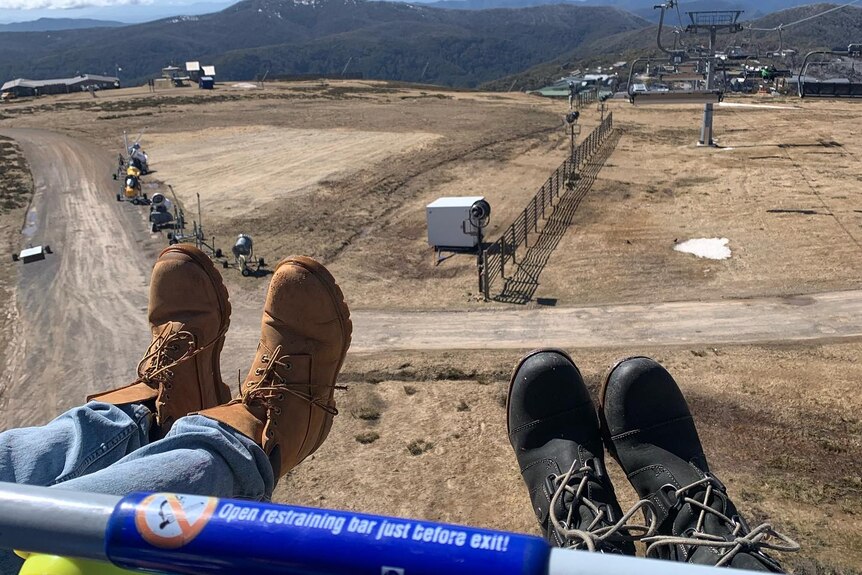 an image of people's boots while they ride a ski lift over a resort that has no snow due to the hot weather