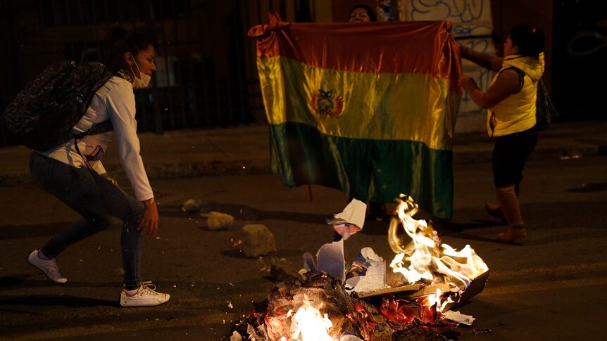 A protester running behind a fire in the streets of Bolivia.