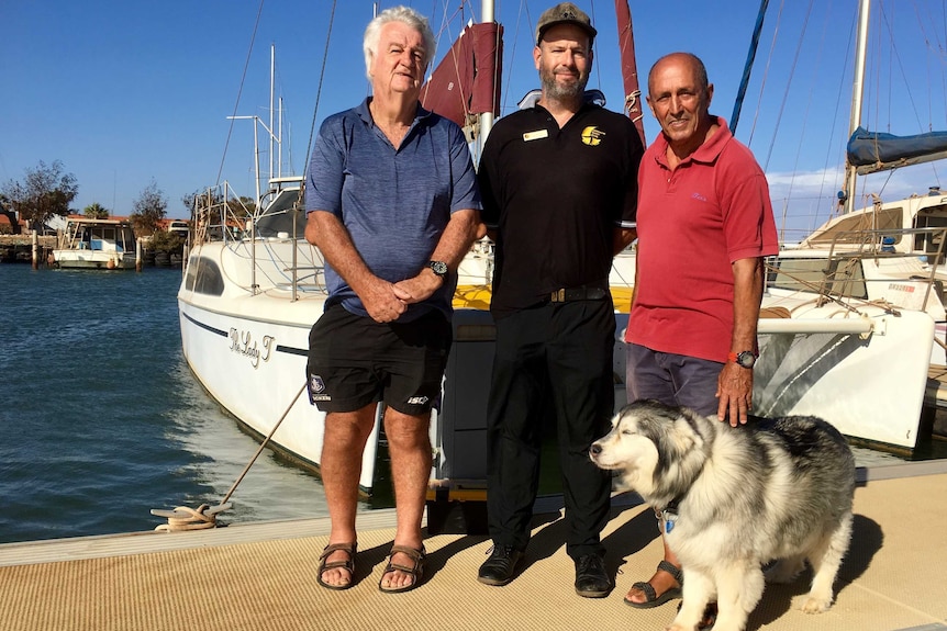 Three men and a dog stand in front of a boat