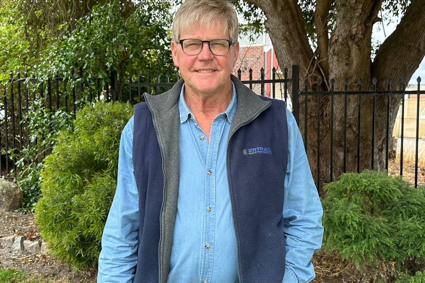 Man in glasses and blue shirt in front of garden and fence