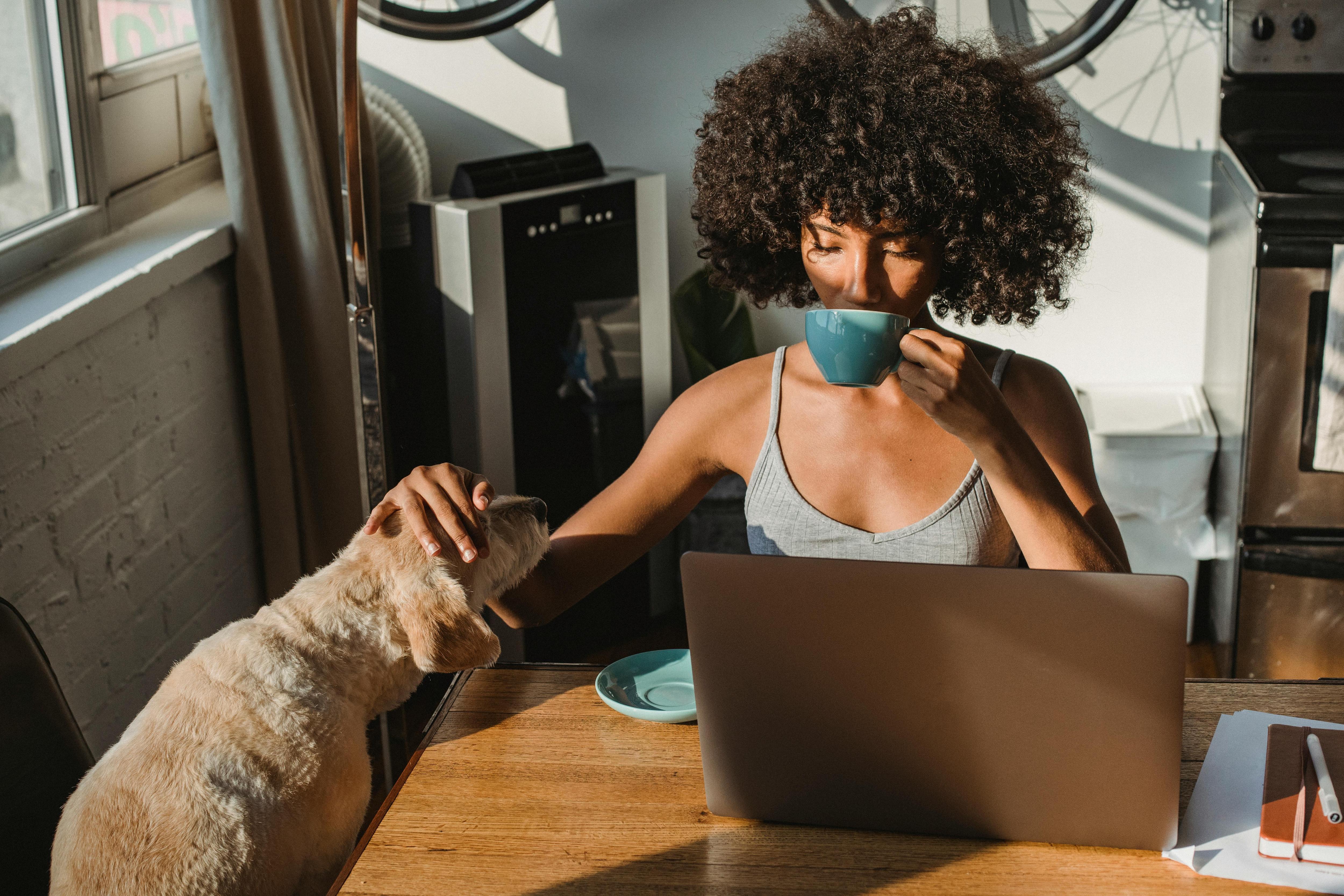 woman sitting at her computer sipping coffee next to dog