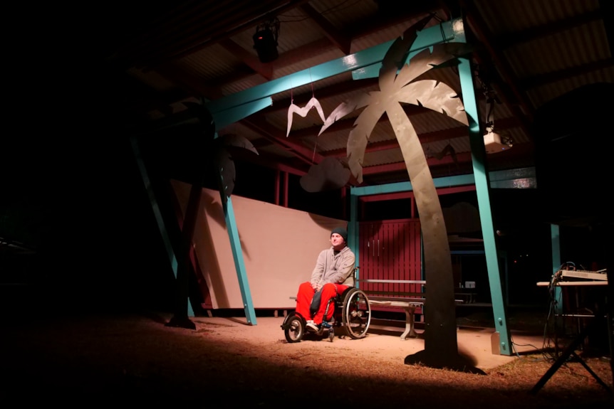 a man sits in a barbecue hut at night time. there are cut outs of trees attached to the hut