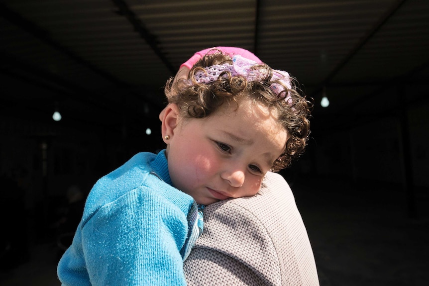 A mother holds her older child while attending the maternity clinic.