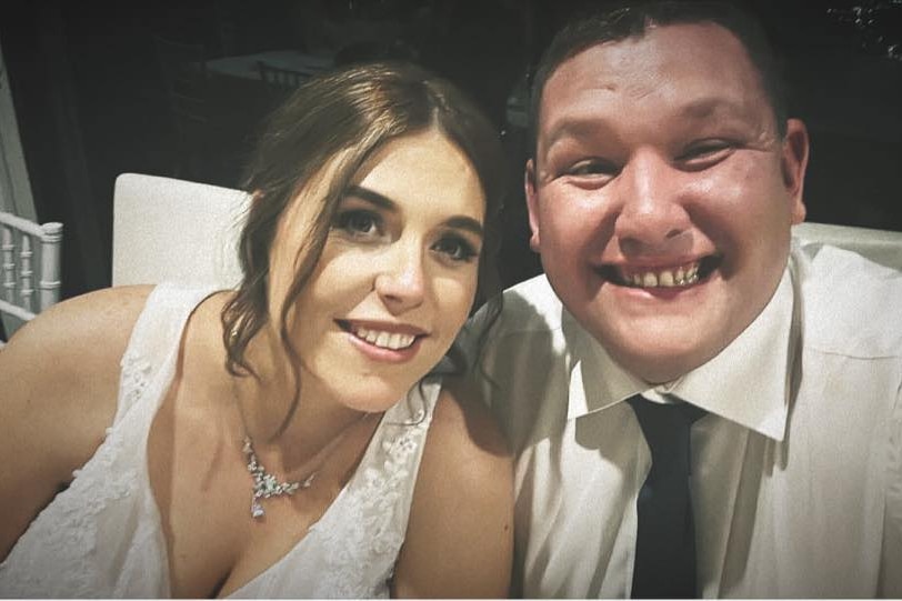 a man smiling sitting next to a woman wearing a wedding dress