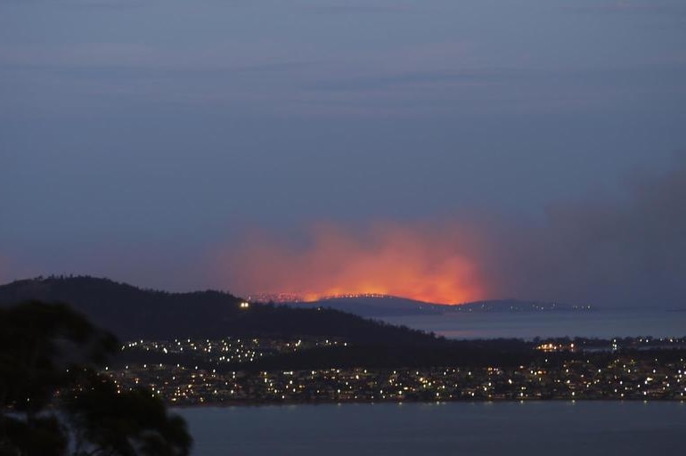 An archival photo shows the city lights of Dunalley with an orange glow surrounding the area