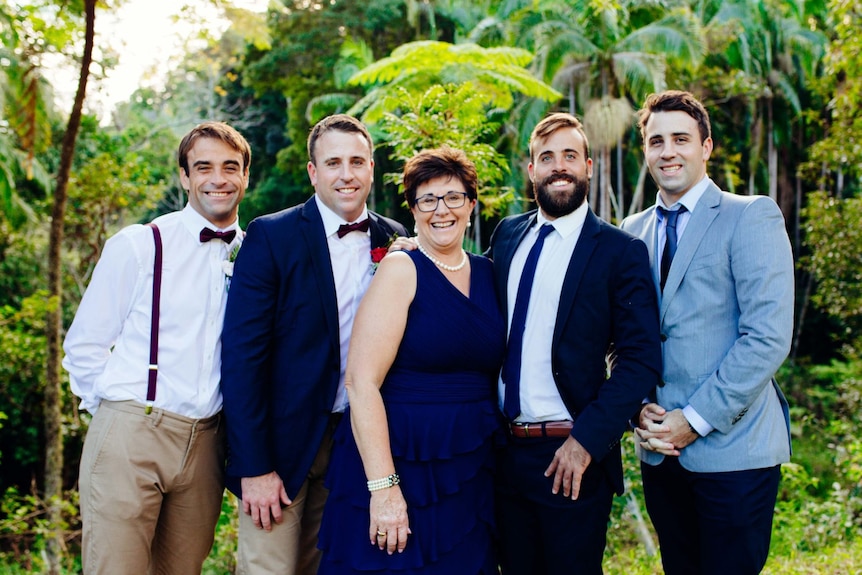 A middle aged woman smiles with four young men in formal outfits