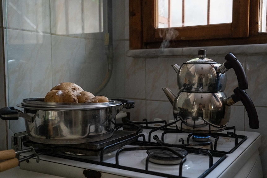 Buhar, bir gaz sobası üzerinde çift istifli bir su ısıtıcısından bir pencereden yükselir.  Bir tencere patates başka bir kazanda