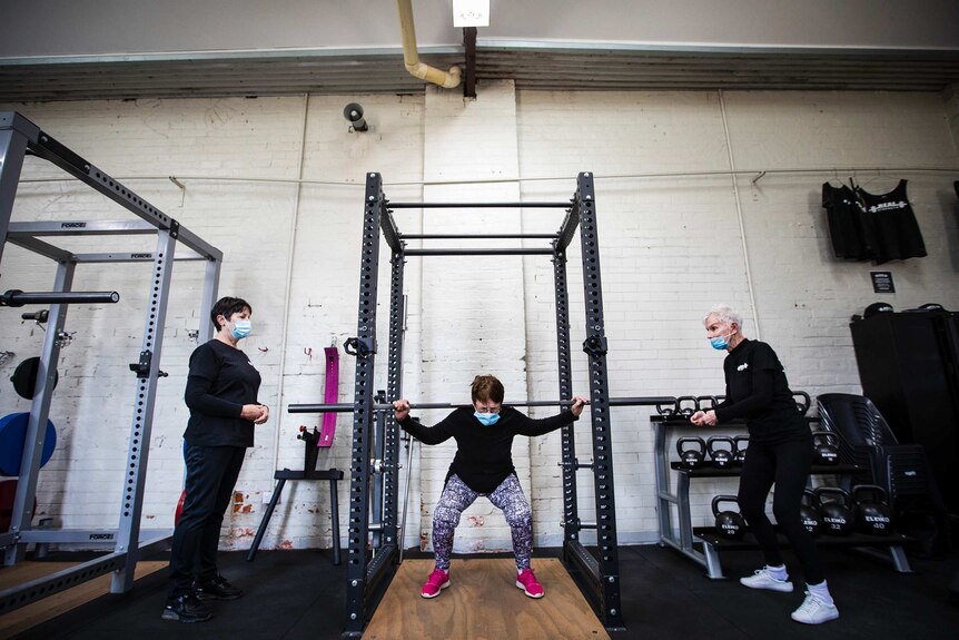 Three women lift weights in a gym