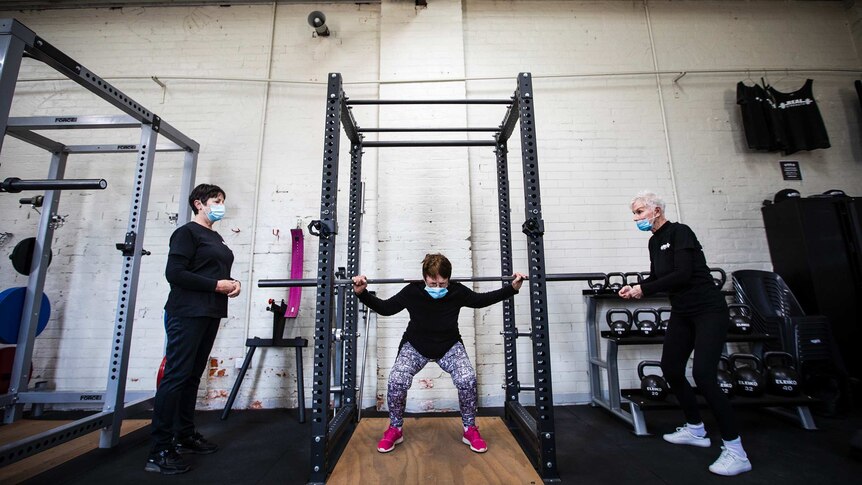 Three women lift weights in a gym