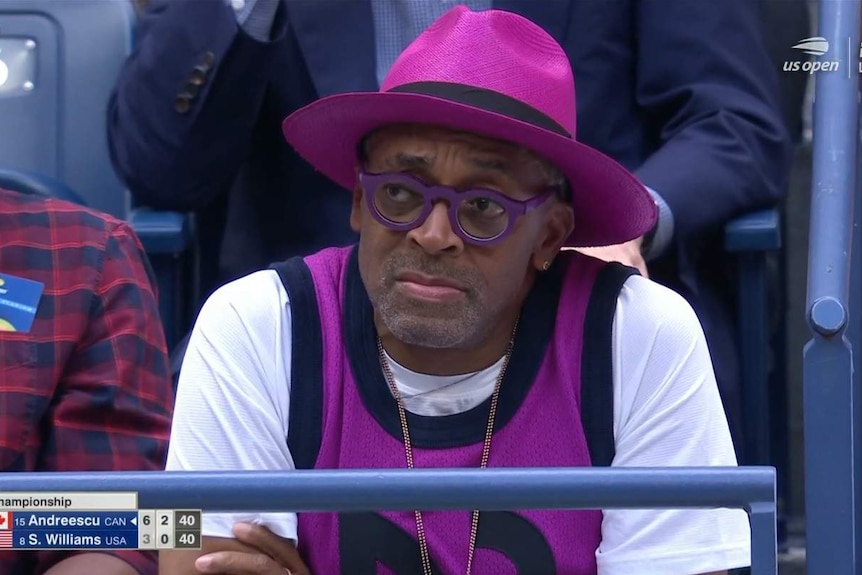 Spike Lee, in a Serena-Williams-purple hat, glasses and vest, looks upset at the US Open
