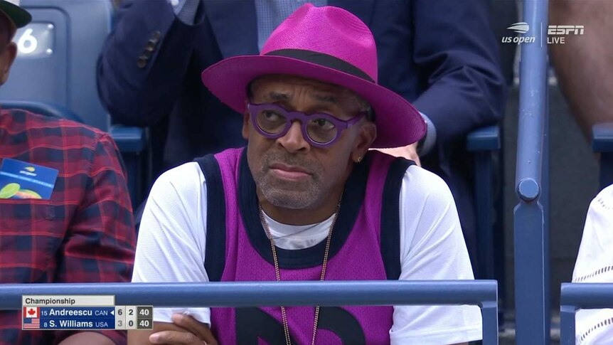 Spike Lee, in a Serena-Williams-purple hat, glasses and vest, looks upset at the US Open