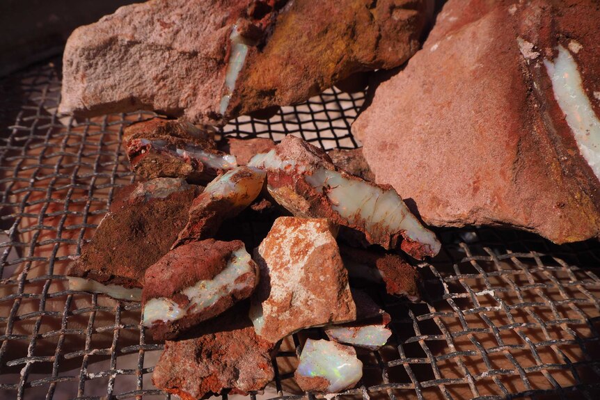 Seams of various colours shine through broken red-brown rocks of varying sizes on a metal grill
