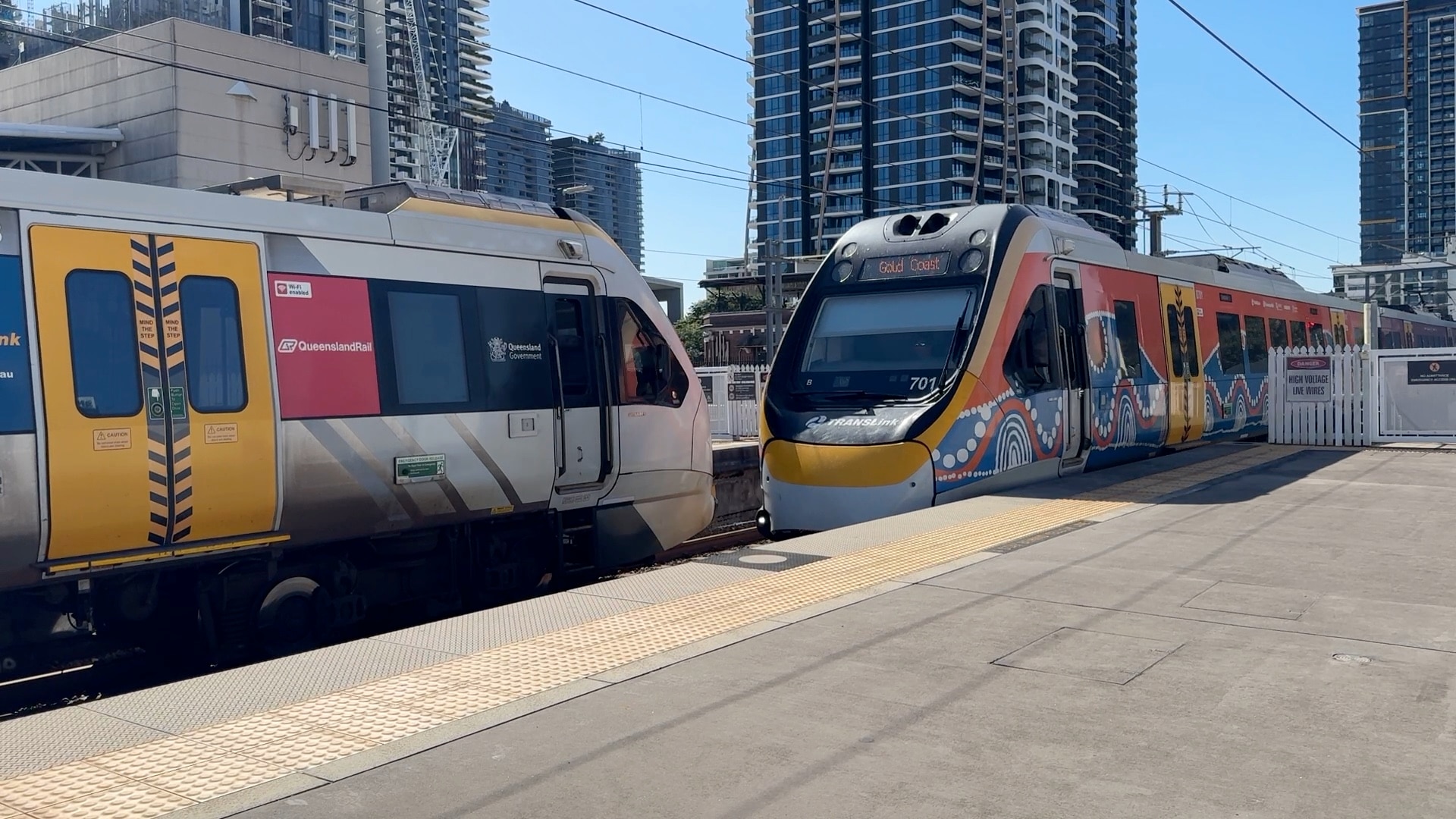 a brightly painted modern train enters a staion with another train on the opposite platform