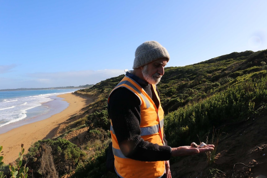 A man wearing a beanie and reflective vest holds shells in his hand.