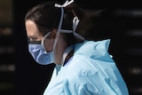 A hospital worker wearing blue scrubs and a face mask.