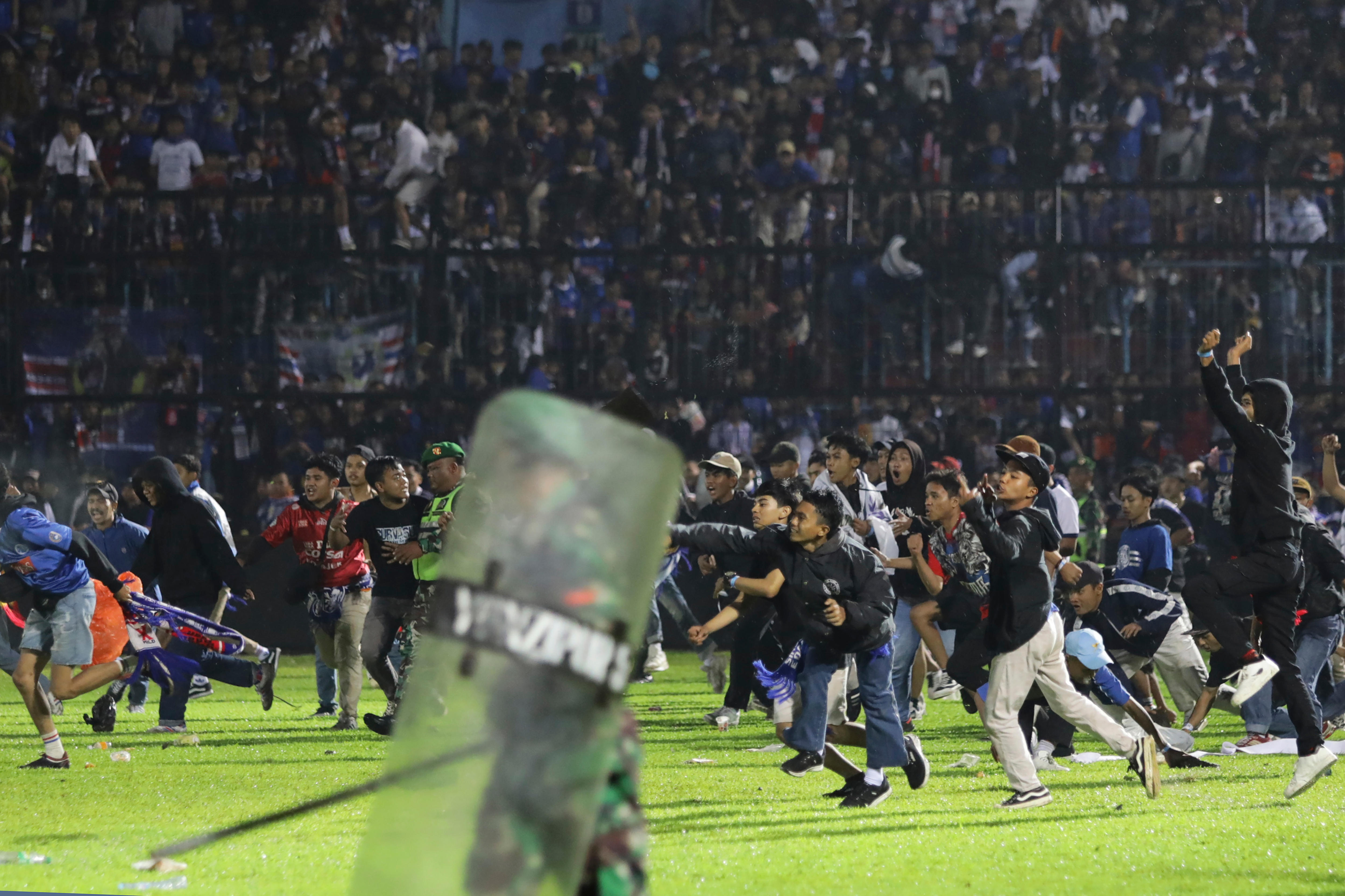 Fans run onto a soccer field as police hold up shields. 
