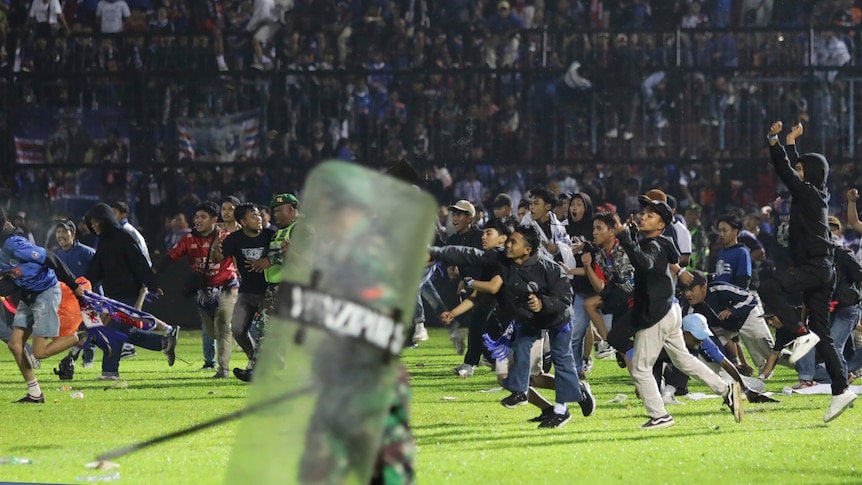 Fans run onto a soccer field as police hold up shields. 