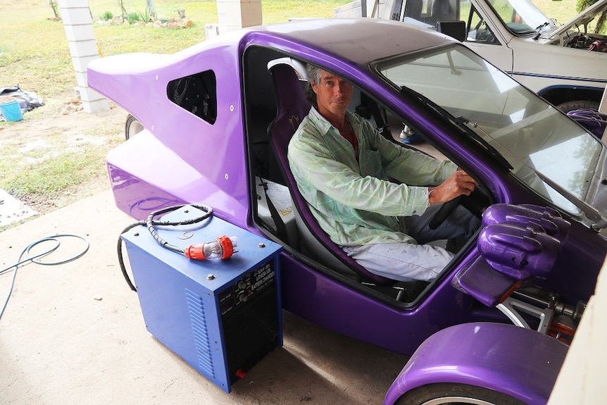 A man sits inside a purple three-wheeled 'trike'