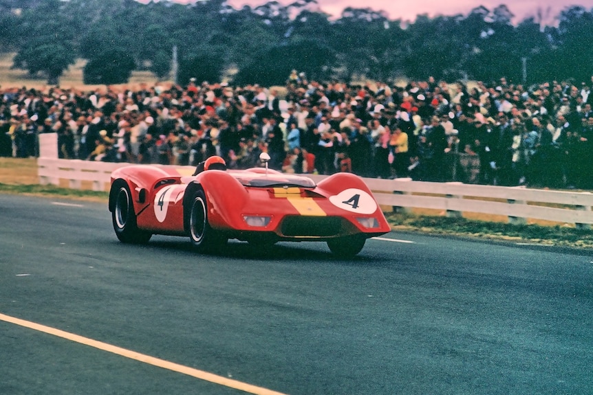 A red race car speeds down a race track as spectators watch.