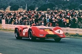 A red race car speeds down a race track as spectators watch.